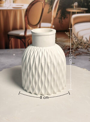 Características clave: Diseño Escultórico Ondulado: Su forma rítmica aporta dinamismo y modernidad, siendo el centro de atención en cualquier repisa, escritorio o mesa de noche. Dimensiones de Proporción Perfecta: Con sus 10 cm de altura, ofrece la estabilidad necesaria para flores de tallo corto o decoraciones con volumen lateral de 8 cm. Acabado Mate Soft-Touch: La superficie de yeso de alta calidad ofrece un tacto suave y una apariencia opaca que transmite serenidad y sofisticación artesanal. Estructura Sólida y Estable: Su base de 8 cm de ancho garantiza que el florero se mantenga firme, soportando el peso de tus creaciones con total seguridad. Material Poroso y Natural: El tono blanco puro del yeso resalta los colores de tus ingredientes botánicos sin competir con ellos. Recomendaciones de uso: Ramos de Jabón de Autor: Utiliza este florero para presentar un mini ramo de Peonias de jabón; las ondas del yeso complementarán perfectamente la textura de los pétalos. Decoración Botánica Seca: Es el soporte ideal para espigas de lavanda, eucalipto preservado o pequeñas ramas de canela, reforzando el concepto de bienestar natural. Personalización Creativa: Al ser de yeso, puedes aplicar técnicas de "decapado" o añadir toques dorados en los bordes de las ondas para un acabado de lujo personalizado. Mantenimiento de la Pieza: Para conservar la blancura impecable, limpia el polvo con una brocha suave de cerdas naturales y evita el contacto directo con agua estancada en el interior si no ha sido sellado previamente.