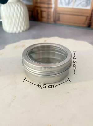 Diseñada con una práctica ventana superior transparente en acetato de alta claridad, este contenedor metálico permite apreciar el color, la textura y los detalles del producto sin necesidad de destaparlo. Su formato perfil bajo es la opción ideal para albergar sólida cera para masajes, bálsamos, velas decorativas (wax melts), jabones artesanales compactos o cosmética sólida.
